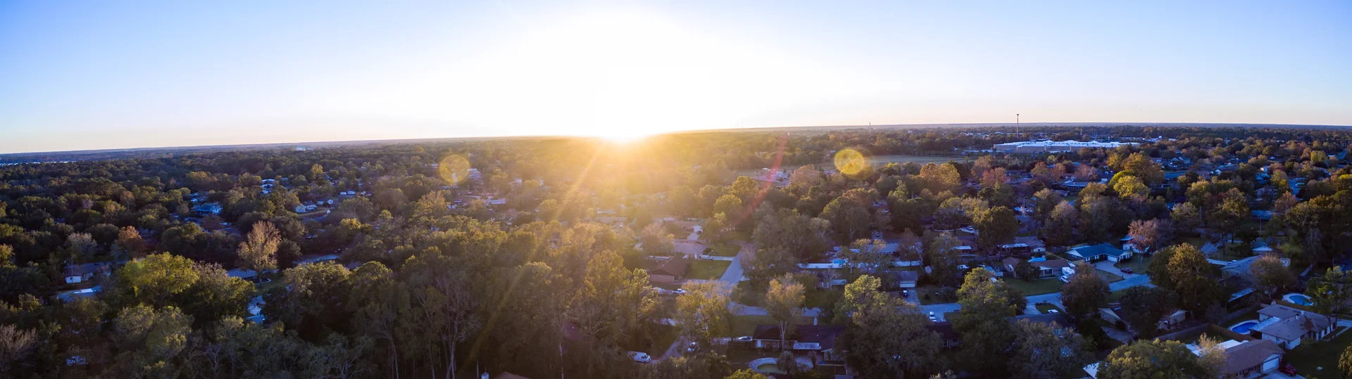 Wide panorama of sunset above a wooded neighborhood.